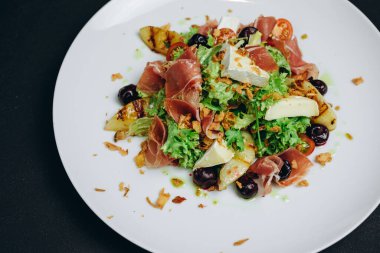 Et ve balık içeren yemek şef tarafından restoranın müşterilerine servis edilir. Beyaz kasede ve siyah masada. Biraz yeşil et ve balık, peynir ve zeytin var. Harika ve mükemmel görünüyor..