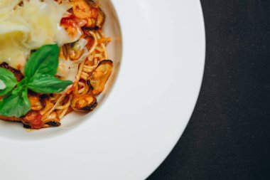 Siyah masada bir kase spagetti var. Siyah masadaki beyaz kasede restoranın yeni ziyaretçileri için yeni bir tabak var. Bir sürü spagetti, biraz yeşil, ketçap ve peynir var. Harika ve harika görünüyor. Mükemmel spagetti.