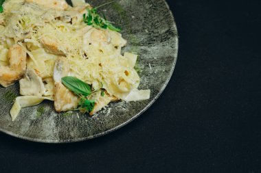 Harika yemek, kafenin siyah masasında servis edilir. Koyu mavi masada bir tabak makarna var. Ziyaretçiler için. Peynirli ve lezzetli görünüyor. Bir sürü spagetti, peynir ve yeşil var..