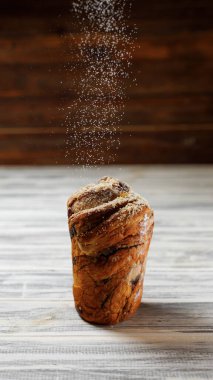 Masada bazı fırınlanmış ürünler var. Birisi üzerine biraz un döküyor. Masa gri..