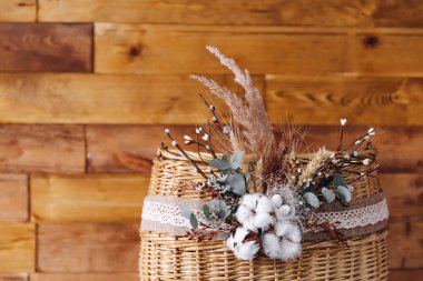Güzel kahverengi arka planda bir Doğu sepeti görebiliyoruz. Üzerinde buğday, dekoratif çiçekler ve yapraklar var. Güzel ve bakımlı görünüyor. Sepetin üzerinde ilginç bir süs var..