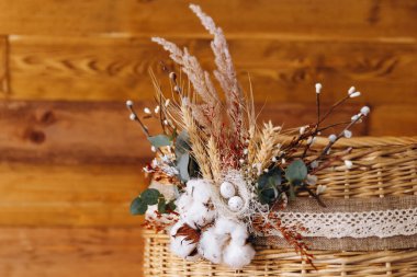 Harika ahşap arka planda bir Doğu sepeti var. Üzerinde buğday, dekoratif çiçekler ve yapraklar var. Güzel ve güzel görünüyor. Sepetin üzerinde ilginç bir süs var..