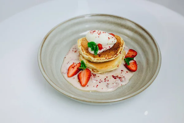 The chef made a new sweet dish for the visitors. There are four strawberries, big pancake and some sauce. It looks tasty, delicious and sweet.