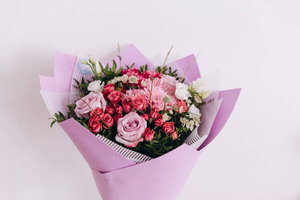 There is a beautiful bouquet of pretty flowers. The bouquet is in a purple-white wrapper on the white background. It is a great present for somebody. It is ready to be bought to the customers.