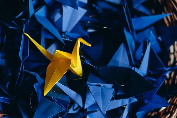 Origami birds made of paper in a basket, one yellow bird among the blue ones