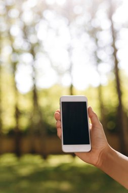 Biri yürüyor ve elinde telefon tutuyor. Arka planda bir park ve bir sürü ağaç da görebiliyoruz. Yürüyüş yaparken telefonunda bir şey yapıyor. Hava güzel..