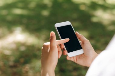 Bir dişi yürüyor ve telefonla bir şeyler yapıyor. Arka planda bir park ve bir sürü ağaç görebiliyoruz. Yürüyüş yaparken telefonunda bir şey yapıyor. Hava güzel..
