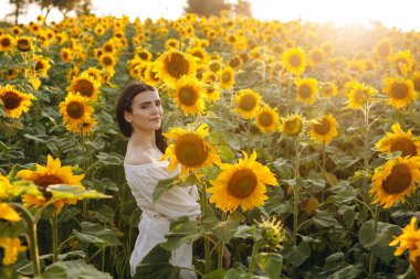 Güzel kız elinde bir ayçiçeği tutuyor. Dişi olan çok güzel. Kızın oldukça koyu bir saçı var. Onun arkasında bir ayçiçeği tarlası var. Bir kızın arkasında bir sürü çiçek görebiliriz..