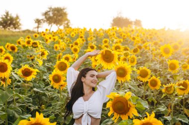 Güzel bayan poz verirken bir şeye bakıyor. Dişi olan güzel ve oldukça koyu renk saçları var. Onun arkasında bir ayçiçeği tarlası var. Arkasında bir gündoğumu görebiliyoruz..