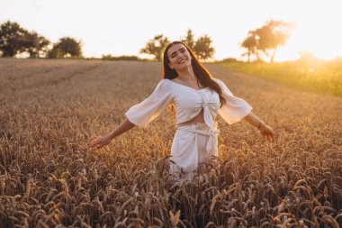 Güzel dişi büyük tarlada eğleniyor ve poz veriyor. Beyaz bir gömlek giyiyor ve harika görünüyor. Güneş ışınlarını görebiliyoruz. Kızın arkasında büyük bir mısır tarlası var..