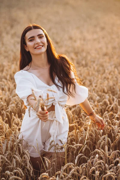 这个面带微笑的女人右手拿着小麦 同时伸出来 她穿着一件白色的衬衫 看上去很迷人 我们可以看到阳光 那姑娘身后有一片大玉米地 — 图库照片