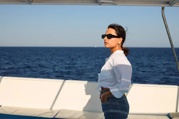 A positive lady walking and enjoying a sea holiday and sun on a boat. Cheerful, smiling, brunette woman in a white blouse, shorts and sunglasses,