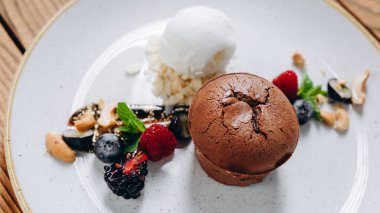 Ahşap masada tatlı görünümlü bir tatlı tabağı var. Tabakta bir pasta, iki çilek, biraz reçel, krema ve fındık görebiliyoruz. İnanılmaz lezzetli görünüyor..