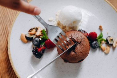 Ahşap masada lezzetli görünümlü bir tatlı tabağı var. Tabakta bir pasta, iki çilek, biraz reçel, krema ve fındık görebiliyoruz. İnanılmaz lezzetli görünüyor..