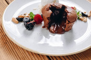 Ahşap masada güzel bir tatlı tabağı var. Tabakta bir pasta, iki çilek, biraz reçel, krema ve fındık görebiliyoruz. İnanılmaz lezzetli görünüyor. Müşteriye servis edilir..