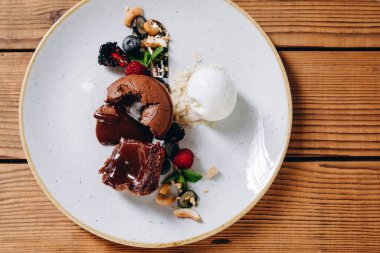 Ahşap masada güzel bir tatlı tabağı görebiliriz. Tabakta bir pasta, iki çilek, biraz reçel, krema ve fındık görebiliyoruz. İnanılmaz lezzetli görünüyor. Müşteriye servis edilir..