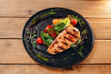 Lezzetli tabağı olan siyah bir tabak var. Domates, kızarmış biftek, biraz yaprak ve yeşil sos görebiliriz. Yemek harika ve lezzetli görünüyor. Müşteriye servis edilir..