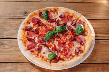 Önümüzde masada leziz peynirli bir pizza görebiliyoruz. Lezzetli pizzada bir sürü sosis, domates, peynir var. Her şey harika görünüyor. Pizza müşteriye servis edilecek..