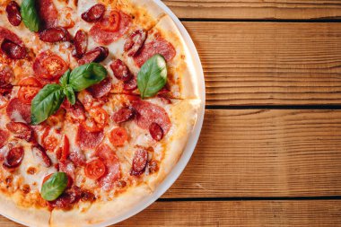 Önümüzde masada peynirli bir pizza görebiliyoruz. Lezzetli pizzada bir sürü sosis, domates, peynir var. Her şey harika görünüyor. Pizza müşteriye servis edilecek..