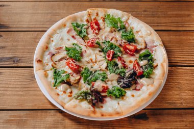 Restoranda küçük bir tabak pizza var. Bir sürü domates, peynir, biraz yaprak ve kızarmış et görebiliriz. Bana çok lezzetli ve harika görünüyor. Tabak masanın üstünde..