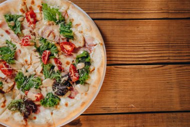 Restoranda bir tabak peynirli pizza var. Bir sürü domates, peynir, biraz yaprak ve kızarmış et görebiliriz. Bana çok lezzetli ve harika görünüyor. Tabak masanın üstünde..