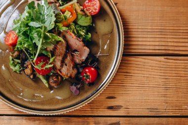 Masanın üzerinde bir garsona yeni bir tabak servis edilir. Bir sürü yeşillik, birkaç domates ve kızarmış et görebiliyoruz. Her şey yağ ile doludur. İlginç ve lezzetli görünüyor..