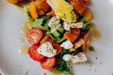 Restoranda yeni bir vejetaryen yemeği var. Bir sürü sebze var, domates, salatalık, biber gibi. Lezzetli görünüyor ve biraz sos ve yağ dökülüyor..