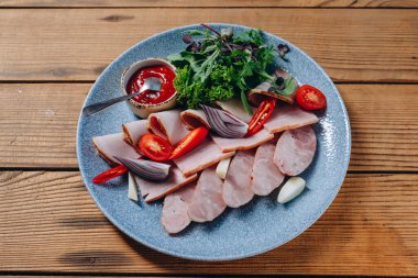 Restoranın ahşap masasında mavi bir sosis tabağı var. Yemekler çok lezzetli ve lezzetli görünüyor. Ayrıca tabakta yeşil, domates dilimleri ve kırmızı sos da görüyoruz..