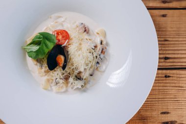 Restoranın ahşap masasında bir tabak hamur ve peynir var. Lezzetli ve lezzetli görünüyor. Ayrıca tabakta bir dilim domates ve tek bir yaprak var. Deniz ürünleri de görüyoruz..