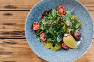 Vejetaryen restoranının masasında mavi bir kase salata var. Çok sağlıklı ve harika görünüyor. Yemek insanlara servis edilir. Kasede bir sürü yaprak ve sebze var..