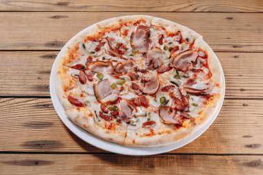 Pizzacının masasındaki beyaz tabakta pizza yiyebiliriz. Lezzetli ve lezzetli görünüyor. Bir sürü et, sosis, salatalık ve peynir görebiliyoruz..