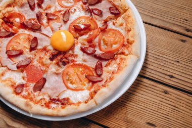 Restoranda yumurtalı bir tabak pizza var. Ortasında yumurta ve harika domates dilimleri olan bir pizza görebiliyoruz. Kızarmış sosis de var ve çok lezzetli görünüyor..