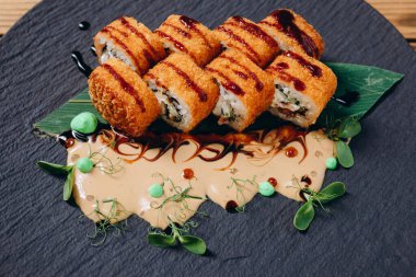 Çin restoranındaki siyah tabakta bir sürü lezzetli yemek dilimleri görebiliyoruz. Harika görünüyor ve sunuluyor. Tabakta soslu bir sürü yaprak var..