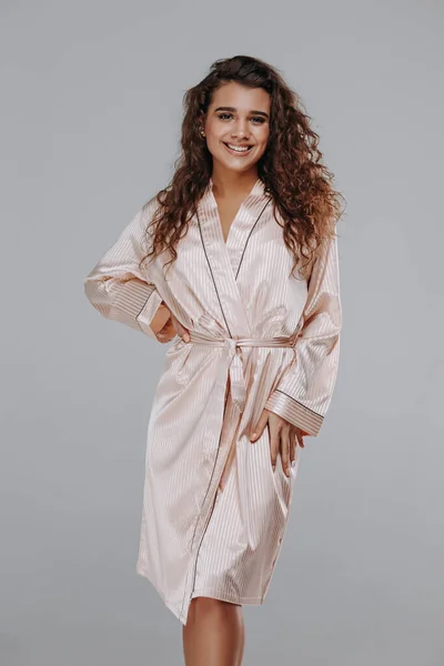 very sexy curly girl in a beige robe, night dress on a gray background. home clothes concept. catalog photo