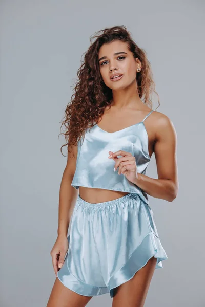very sexy curly girl in a blue pajama, night clothes on a gray background. home clothes concept. catalog photo. pajama shorts and top
