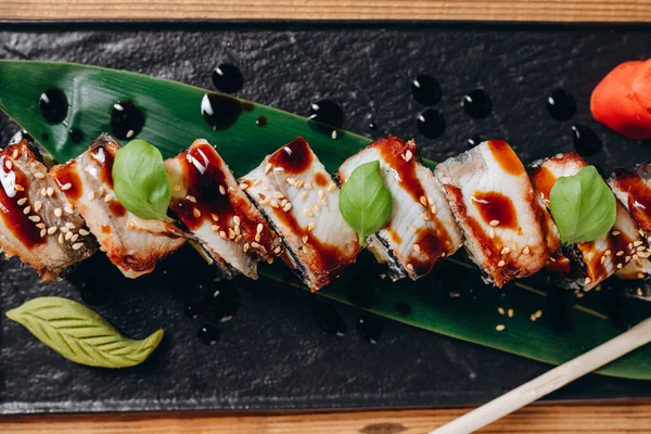 stock image There are a new type of sushi in the restaurant. There are a lot of sauce and small leafs on the black rectangular plate on the wooden table. It looks great and tasty. Sushi are placed on the leaf.