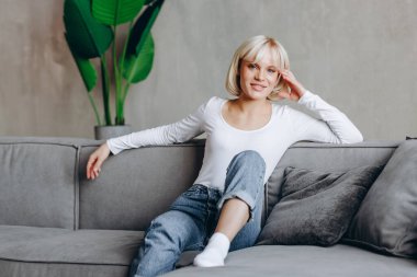 Güzel sarışın kız koltukta oturuyor ve kameraya bakıyor..