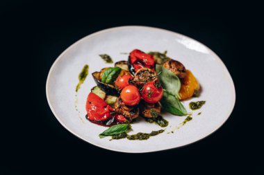 Siyah arka planda izole edilmiş, beyaz tabakta ızgara sebzeler..