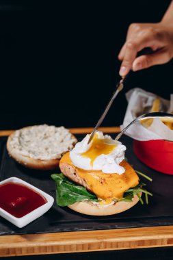 Sulu burger, haşlanmış yumurta, somon bifteği ve çedar peyniri. Aşçı haşlanmış yumurta keser, yumurta sarısı akar..