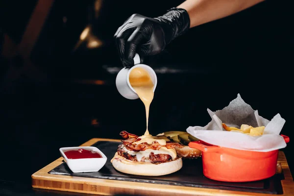 Barbekü soslu ve kızarmış patatesli leziz bir domuz pastırmalı çizburger. Şef burgerin üzerine peynir sosu döker..
