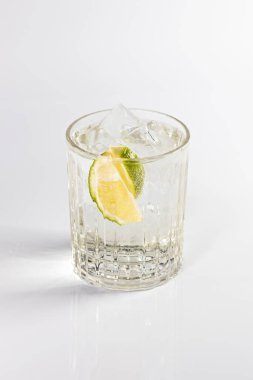 Koyu bir bardakta limon ve buzla süslenmiş cin ve tonik kokteyli. Beyaz arkaplanda izole.