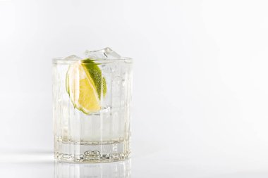 Koyu bir bardakta limon ve buzla süslenmiş cin ve tonik kokteyli. Beyaz arkaplanda izole.