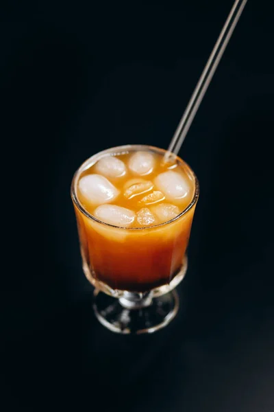 A glass of iced black coffee and layer of orange and lemon juice on black background.