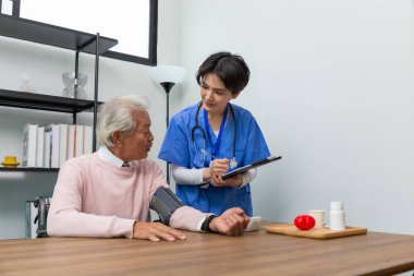 Dost canlısı personel ve kıdemli adam kan basıncını ve kalp atışlarını evde dijital basınç göstergesiyle kontrol ediyor. Yaşlı kadın sağlığıyla ilgileniyor. Sağlık ve Tıp Konsepti.