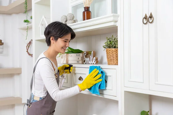 stock image Woman cleaning dust from bookshelf. Young girl sweeping shelf in living room.