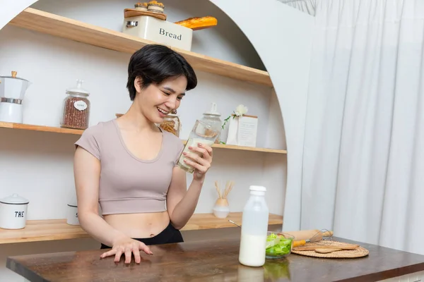 アジアの若い美しい女性が自宅でキッチンで牛乳を飲んでいます ヘルスケアの概念 — ストック写真