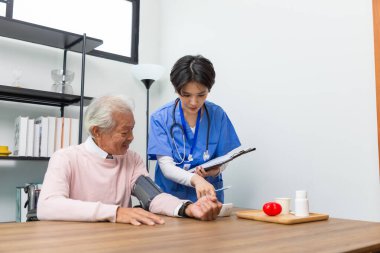 Dost canlısı personel ve kıdemli adam kan basıncını ve kalp atışlarını evde dijital basınç göstergesiyle kontrol ediyor. Yaşlı kadın sağlığıyla ilgileniyor. Sağlık ve Tıp Konsepti.