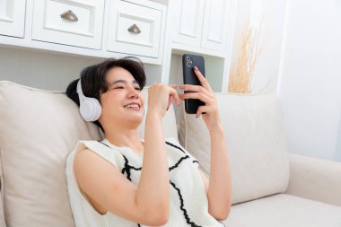 Elinde telefon olan güzel bir bayanın, rahat koltukta oturan kulaklıklarıyla modern bir şarkıyı açtığı fotoğraf..