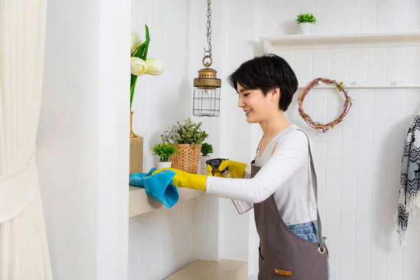 Young woman cleaning her house, she is dusting a shelf, chores and hygiene concept