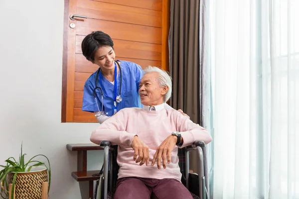 Friendly staff caregiver of nursing home talking to asian senior man in living room